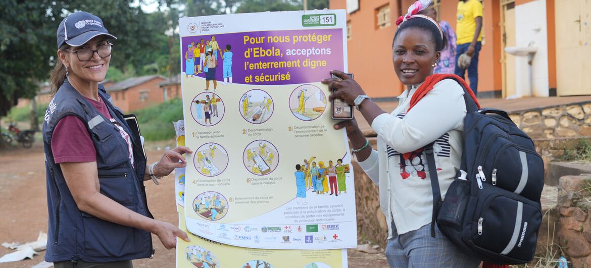 Un agent de santé de l'OMS et une femme de la région brandissent une grande affiche d'information sur la prévention d'Ebola et les pratiques funéraires dignes à Nyankunde, dans l'Ituri, en République démocratique du Congo.