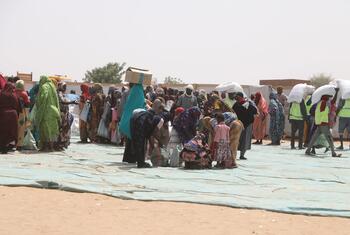 Women and aid workers at a food distribution site in Adre, Chad. Refugees receive bags of food aid from the World Food Programme (WFP) in the desert.