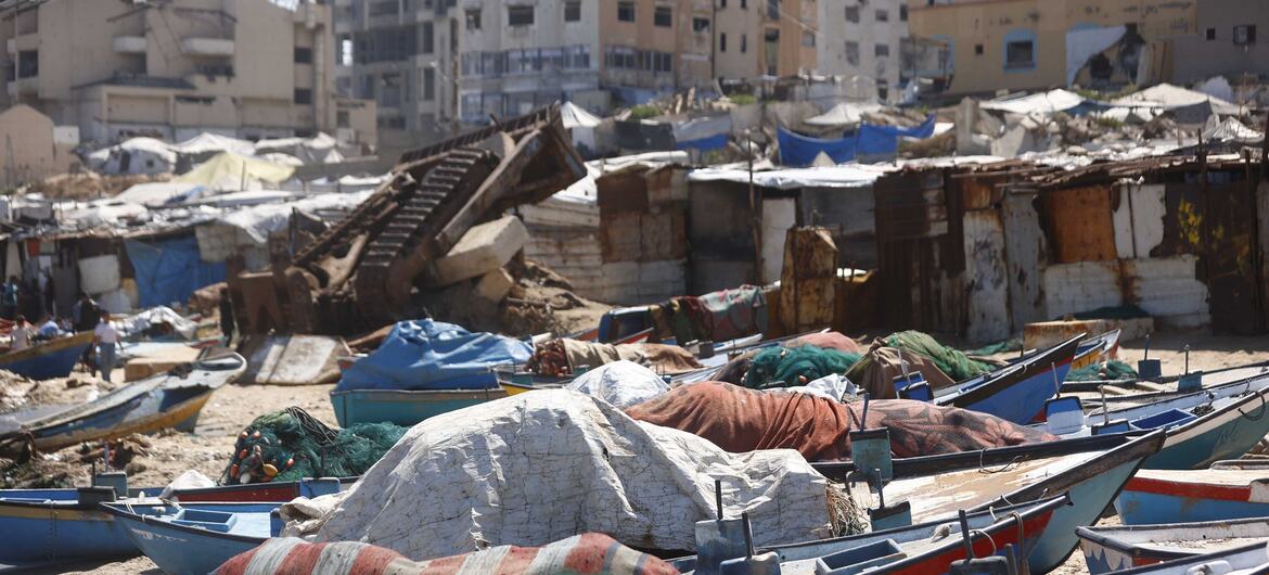 Tents housing displaced Palestinians stretch out amidst moored boats and burnt-out structures in Gaza.