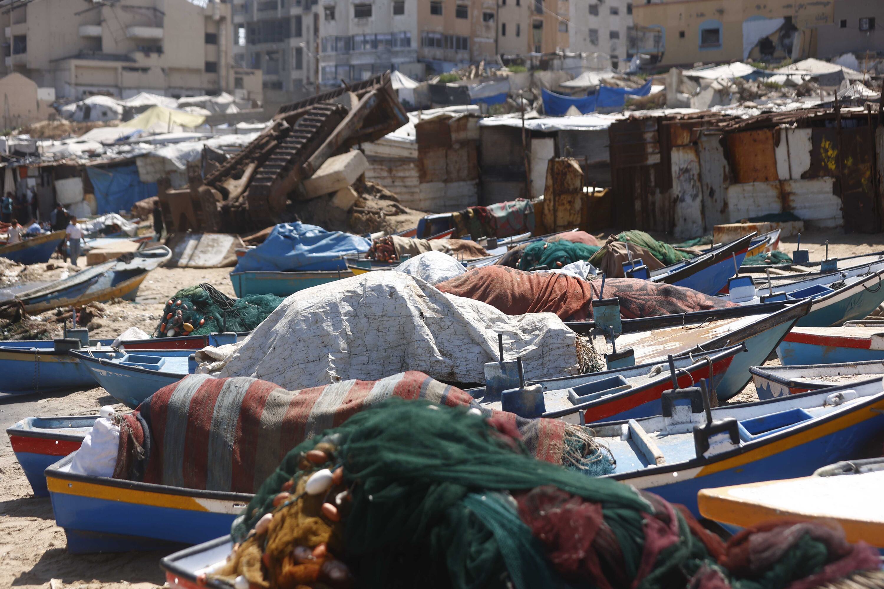 تنتشر الخيام التي تؤوي الفلسطينيين النازحين وسط القوارب الراسية والمباني المحترقة في غزة.