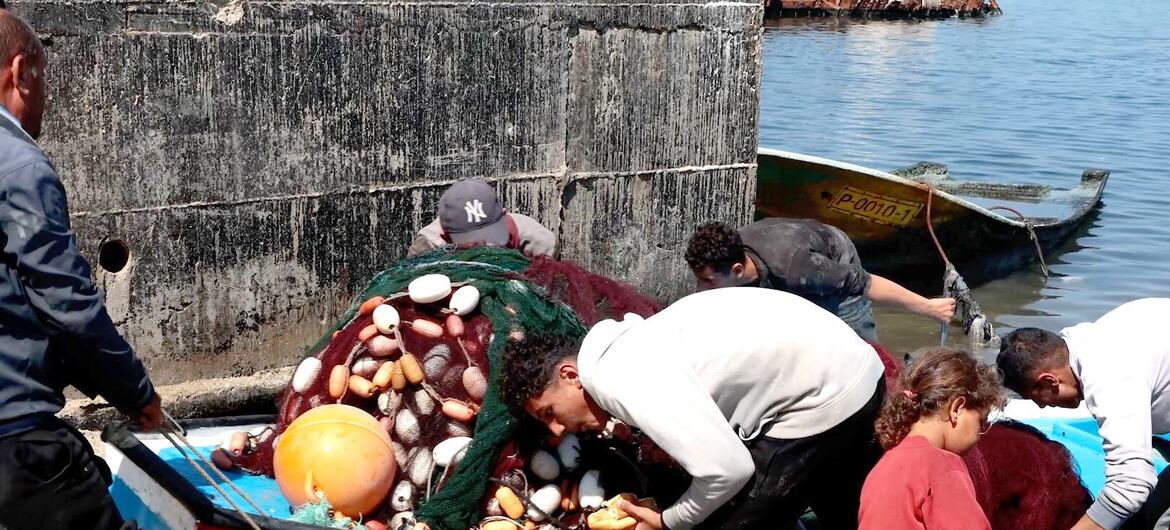 يقوم صيادو غزة بسحب قارب الصيد الخاص بهم إلى الشاطئ.