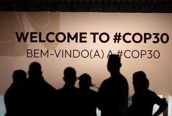 صور ظلية لأشخاص يقفون أمام لافتة كبيرة كُتب عليها "مرحباً بكم في #COP30" و "BEM-VINDO(A) A #COP30" في فعالية UNFCCC في بيليم.