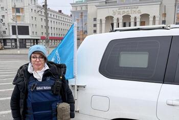 La trabajadora de seguridad de la ONU, Olga Scripovaisa, se encuentra en una calle de Odesa, Ucrania, junto a un vehículo de la ONU con la bandera azul de la ONU a la vista.