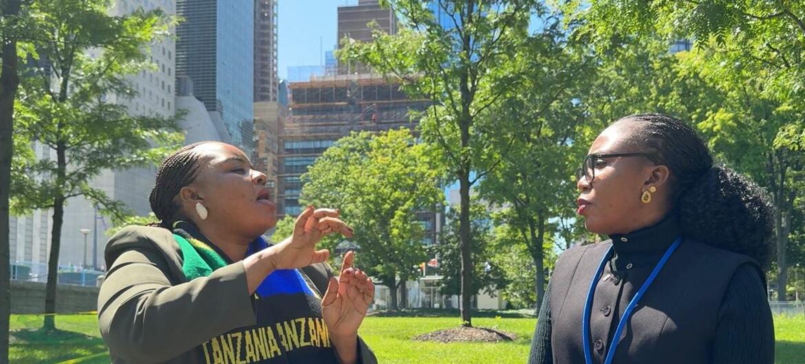 Wanawake wawili wamekaa kwenye benchi la bustani mjini, mmoja akizungumza kwa lugha ya ishara huku mwingine akisikiliza kwa makini.