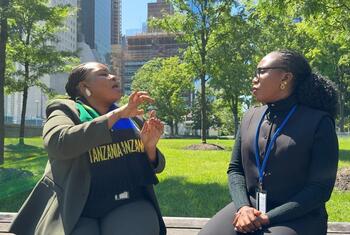 Wanawake wawili wamekaa kwenye benchi la bustani mjini, mmoja akizungumza kwa lugha ya ishara huku mwingine akisikiliza kwa makini.