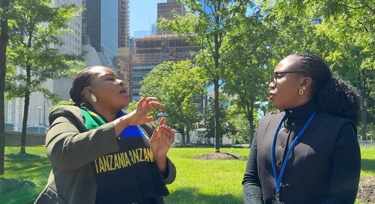 Wanawake wawili wamekaa kwenye benchi la bustani mjini, mmoja akizungumza kwa lugha ya ishara huku mwingine akisikiliza kwa makini.