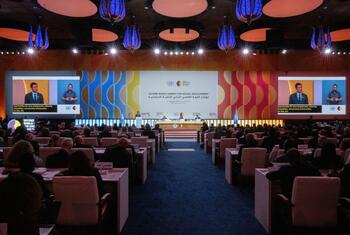 A large conference hall during the Second World Summit for Social Development, with a speaker at a podium and a large screen displaying the event title and a presentation.