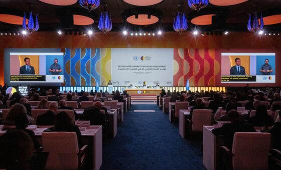 A large conference hall during the Second World Summit for Social Development, with a speaker at a podium and a large screen displaying the event title and a presentation.