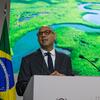 Um homem de terno e óculos discursa em um pódio na conferência COP30, com as bandeiras da ONU e do Brasil atrás dele.