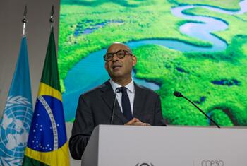 Um homem de terno e óculos discursa em um pódio na conferência COP30, com as bandeiras da ONU e do Brasil atrás dele.