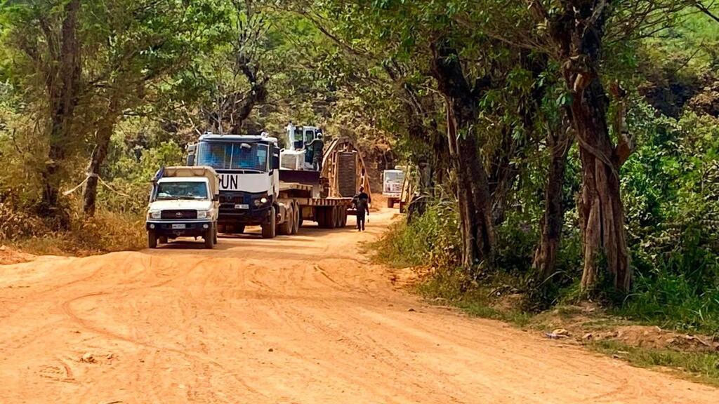 Un convoi de véhicules, dont un camion de ONU , circule sur une piste de terre à travers une forêt de la République démocratique du Congo.