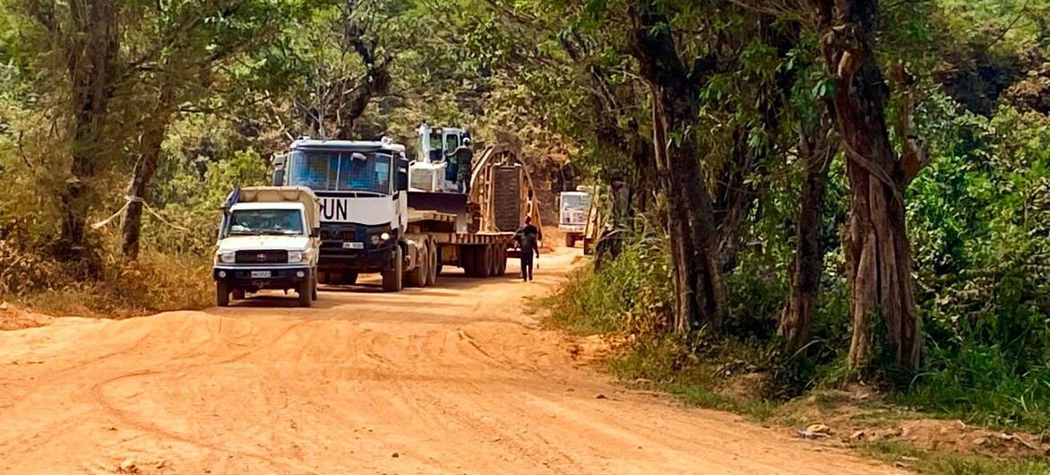 Un convoi de véhicules, dont un camion de ONU , circule sur une piste de terre à travers une forêt de la République démocratique du Congo.
