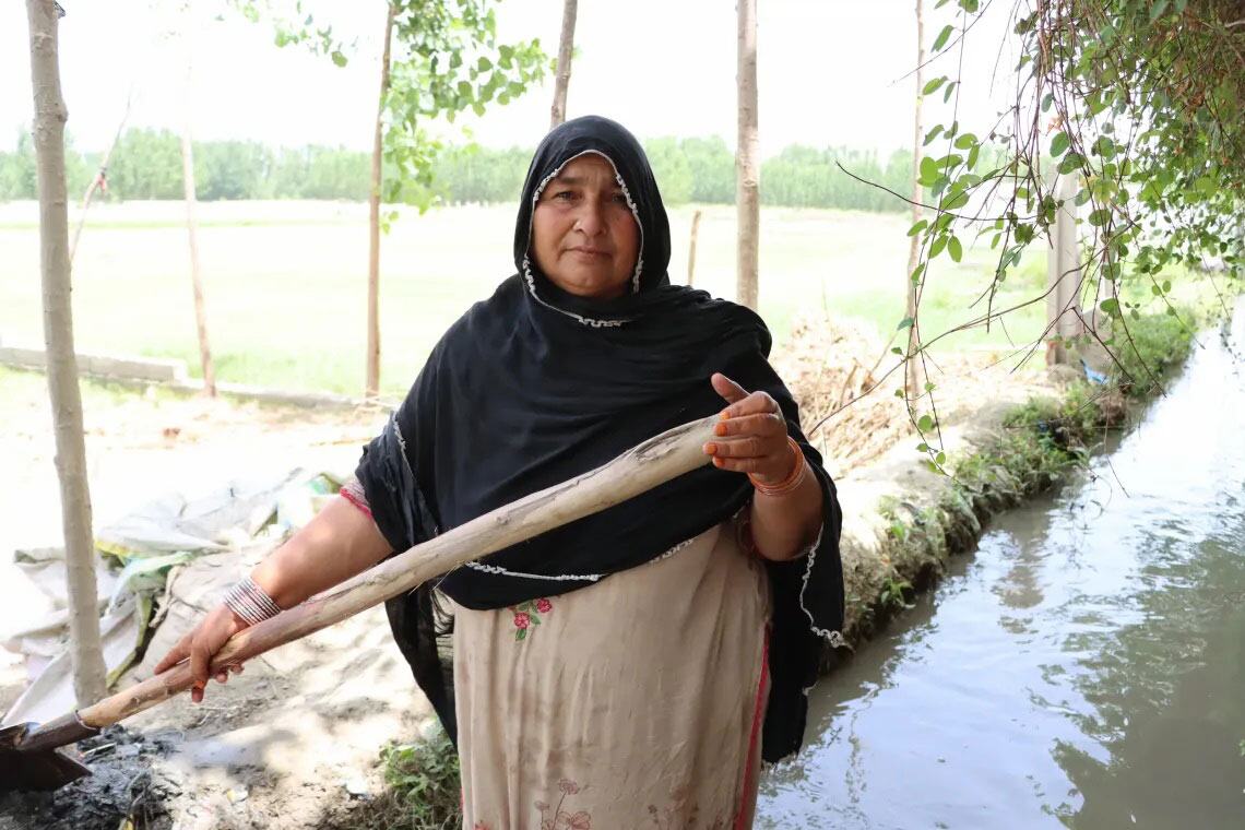 پاکستان میں ایک خاتون بیلچہ پکڑے ایک نہر کے کنارے کھڑی ہے، برطانیہ کی حکومت اور UNICEF کے تعاون سے بچوں کے تحفظ کے ایک سماجی اقدام میں حصہ لے رہی ہے۔