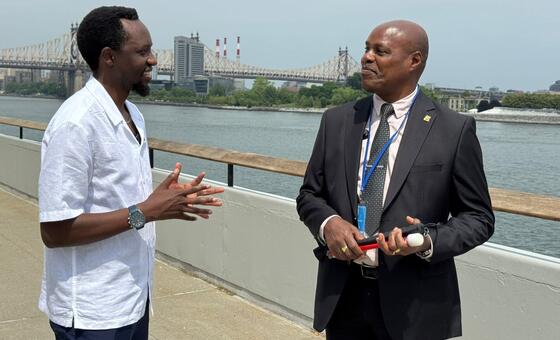 Wanaume wawili wanazungumza kwenye sehemu ya kupumzikia ufukweni huku Daraja la Queensboro likiwa nyuma. Mwanamume wa kushoto amevaa shati jeupe, huku mwanamume wa kulia amevaa suti na ameshika fimbo nyeupe.