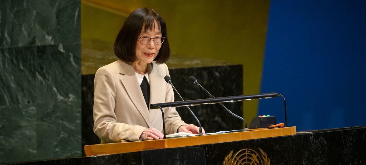 Japanese woman Tomoko Akane speaks at a podium bearing the United Nations emblem.