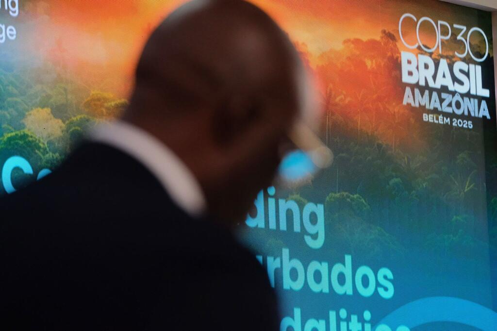 Um delegado na cúpula climática COP30 em Belém, Brasil, está em frente a um painel promocional do evento.