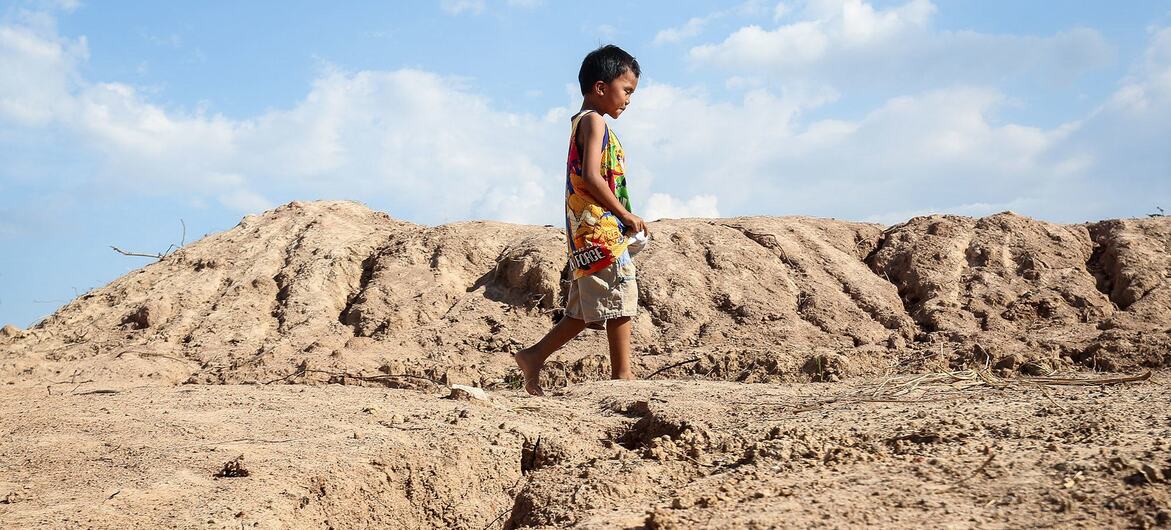 A young boy walks barefoot across a dry, eroded landscape in Thailand.