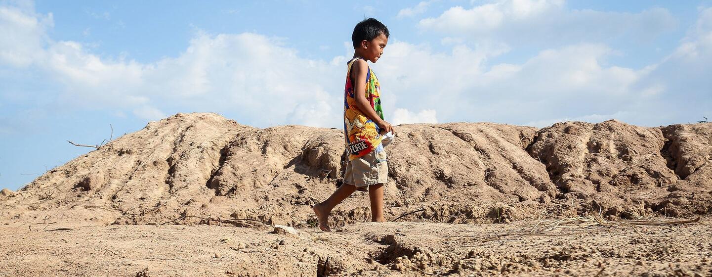 Un jeune garçon marche pieds nus à travers un paysage aride et érodé en Thaïlande.