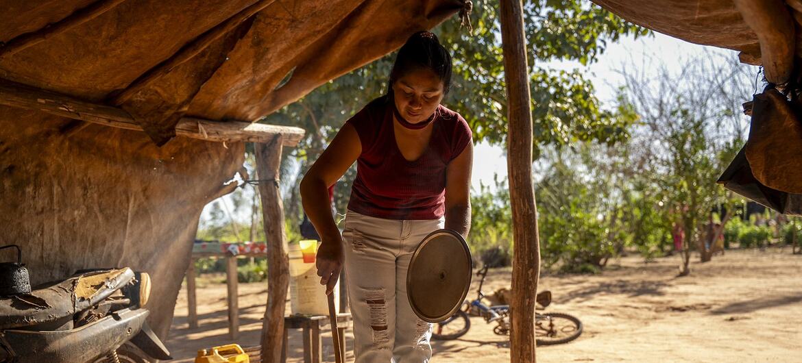En una zona rural de Paraguay, una mujer cocina a fuego abierto en una cocina al aire libre, utilizando una olla grande y una cuchara de madera.