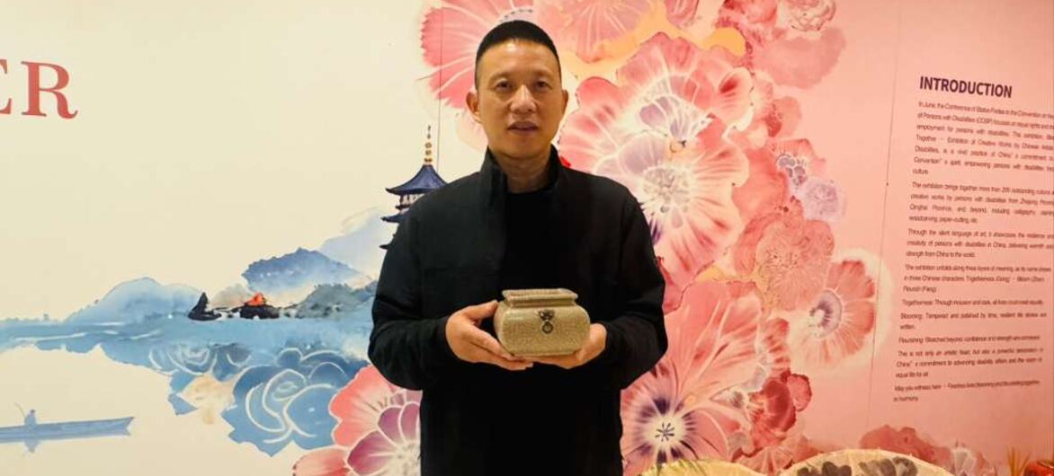 一名男子站在一面装饰着粉红色大花的展览墙前，手里拿着一个陶瓷罐。