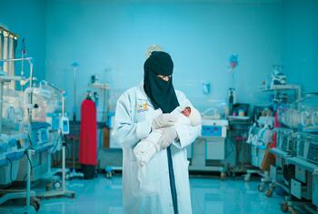 A midwife in a white coat and black hijab holds a newborn baby in a neonatal intensive care unit in Marib, Yemen.
