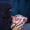 امرأة في اليمن ترتدي النقاب تحمل طفلا حديث الولادة ملفوفا ببطانية.