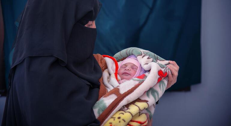 امرأة في اليمن ترتدي النقاب تحمل طفلا حديث الولادة ملفوفا ببطانية.