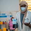 Dans une clinique, Sadio Yalcouye, nutritionniste malien portant un masque et un foulard, tient deux boîtes de compléments alimentaires F-100 et F-75.