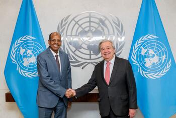 UN Secretary-General António Guterres and Youssouf shake hands in front of the UN emblem and two UN flags.