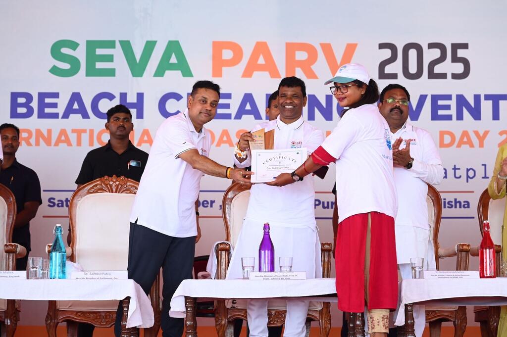 भारत में आयोजित सेवा पर्व 2025 बीच क्लीनिंग इवेंट में, सफेद वर्दी पहने एक व्यक्ति सफेद शर्ट और लाल स्कर्ट पहने एक महिला को प्रमाण पत्र प्रदान करता है।
