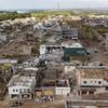 Vista aérea de uma cidade brasileira devastada por um tornado, mostrando destruição generalizada com prédios desabados e destroços espalhados pelas ruas.