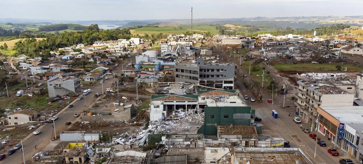 Vista aérea de uma cidade brasileira devastada por um tornado, mostrando destruição generalizada com prédios desabados e destroços espalhados pelas ruas.