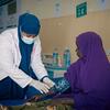 A female healthcare worker in a white coat and blue hijab takes a patient's blood pressure in a clinic in Somalia.