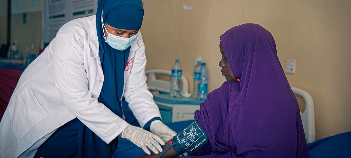 Una trabajadora sanitaria, vestida con bata blanca y hiyab azul, toma la presión arterial de un paciente en una clínica de Somalia.
