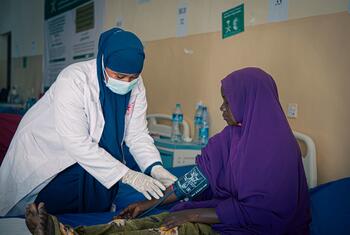 A female healthcare worker in a white coat and blue hijab takes a patient's blood pressure in a clinic in Somalia.