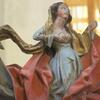 Primer plano de una escultura de madera que representa a una mujer con un vestido azul con drapeados rojos y dorados, posiblemente una figura religiosa.