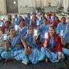 Um grupo de mulheres indianas em uma sessão de treinamento, cada uma segurando um smartphone exibindo a interface de um aplicativo.