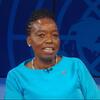 Monic Juma, mwanamke aliyevaa fulana ya bluu, akizungumza kwenye jukwaa mbele ya nembo ya UNODC huko Vienna.
