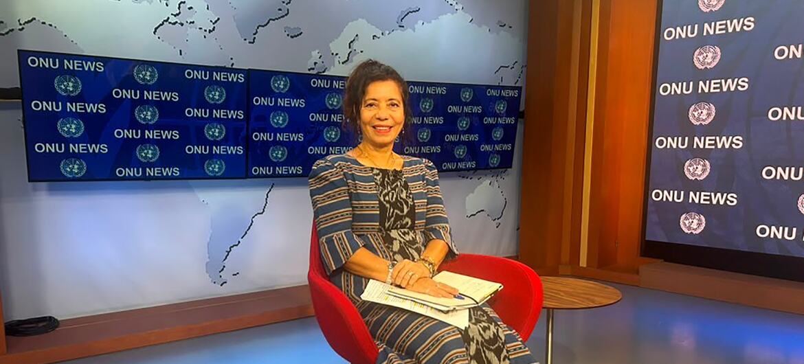 A apresentadora de notícias Céu Brites, de Timor-Leste, está sentada em uma cadeira vermelha em um estúdio de notícias, com a marca 'ONU NEWS' e um mapa-múndi ao fundo.