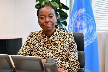 UNODC Executive Director Monica Juma seated at her desk with a UN flag in the background on her first day in office.