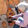 الفنانة الفلسطينية جنى أبو حربيد ترسم جدارية على جدار في غزة تصور منزل عائلة وخيمة.
