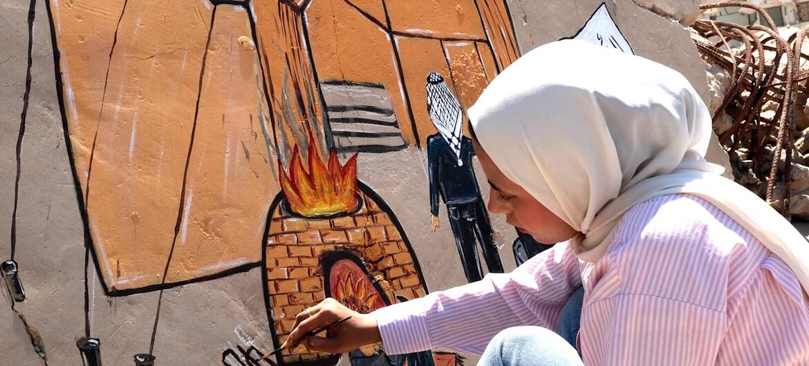 الفنانة الفلسطينية جنى أبو حربيد ترسم جدارية على جدار في غزة تصور منزل عائلة وخيمة.