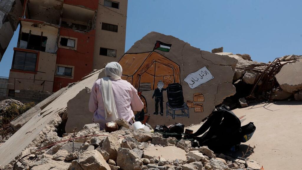 Une Palestinienne observe une fresque peinte sur un morceau de gravats, représentant une tente ornée d'un drapeau palestinien.