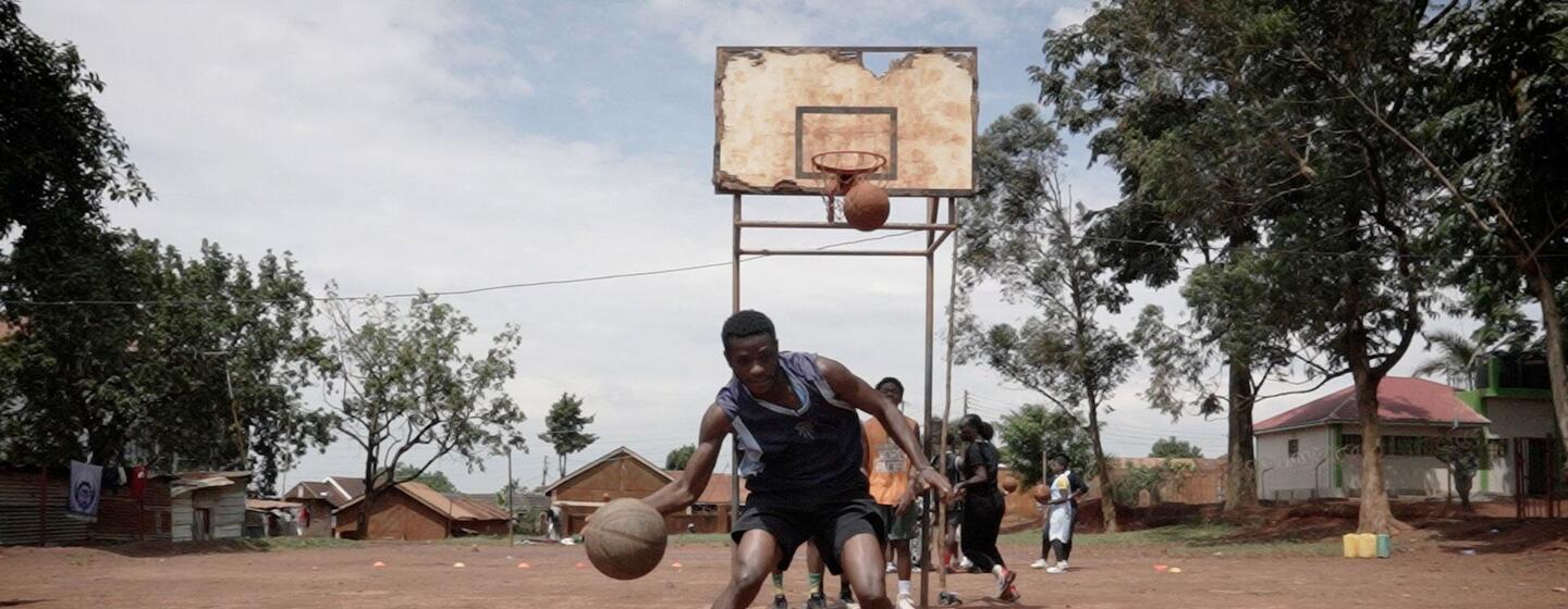 Un grupo de jugadores de baloncesto refugiados de la República Democrática del Congo y jóvenes de Uganda posan para una foto de equipo en una cancha de baloncesto frente a un edificio con la inscripción "Don Bosco".