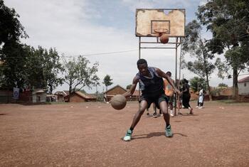 Un grupo de jugadores de baloncesto refugiados de la República Democrática del Congo y jóvenes de Uganda posan para una foto de equipo en una cancha de baloncesto frente a un edificio con la inscripción "Don Bosco".
