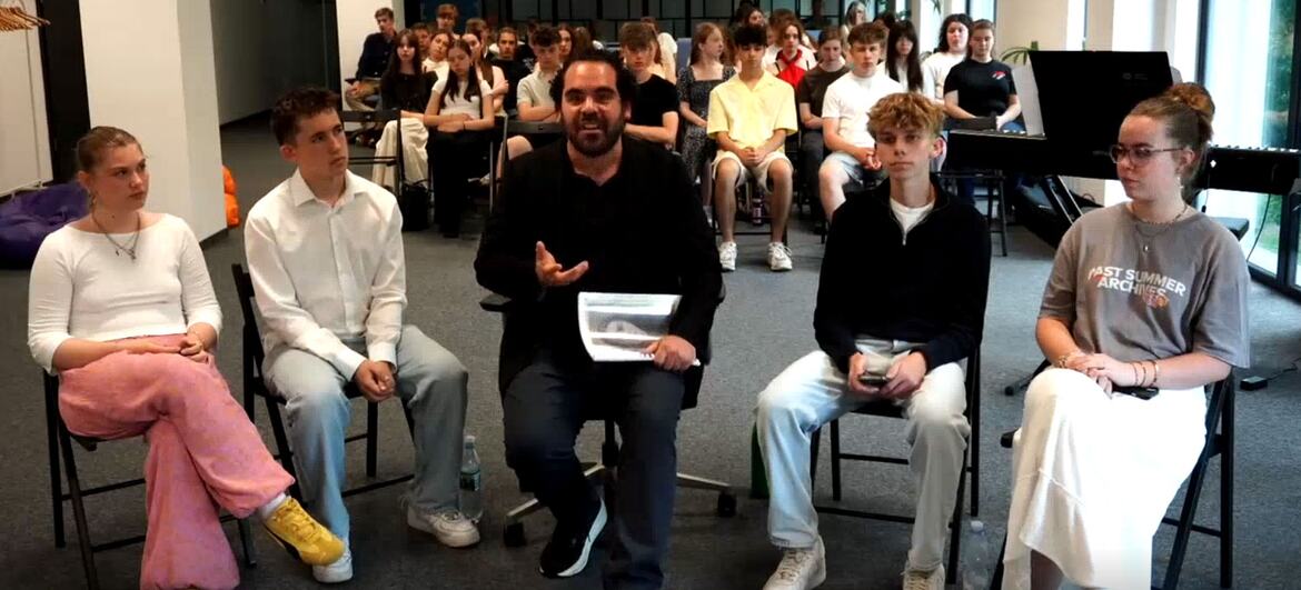 A man speaking to an audience during a UN discussion series, with a panel of young people seated in the foreground.