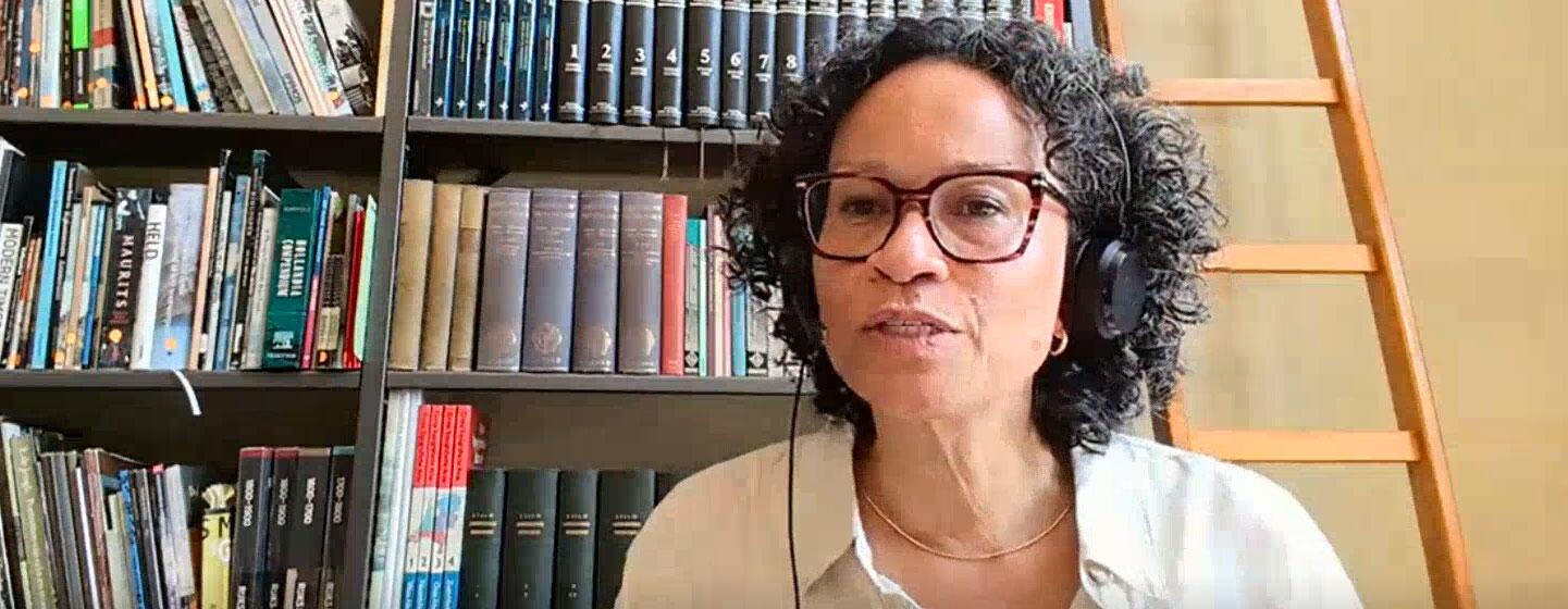 Valika Smeulders, portant un casque et des lunettes, prend la parole lors d'une discussion en direct devant une bibliothèque.