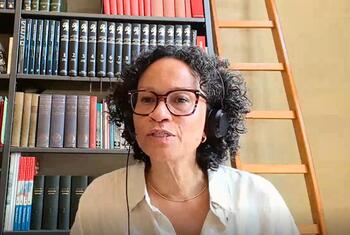 Valika Smeulders, portant un casque et des lunettes, prend la parole lors d'une discussion en direct devant une bibliothèque.