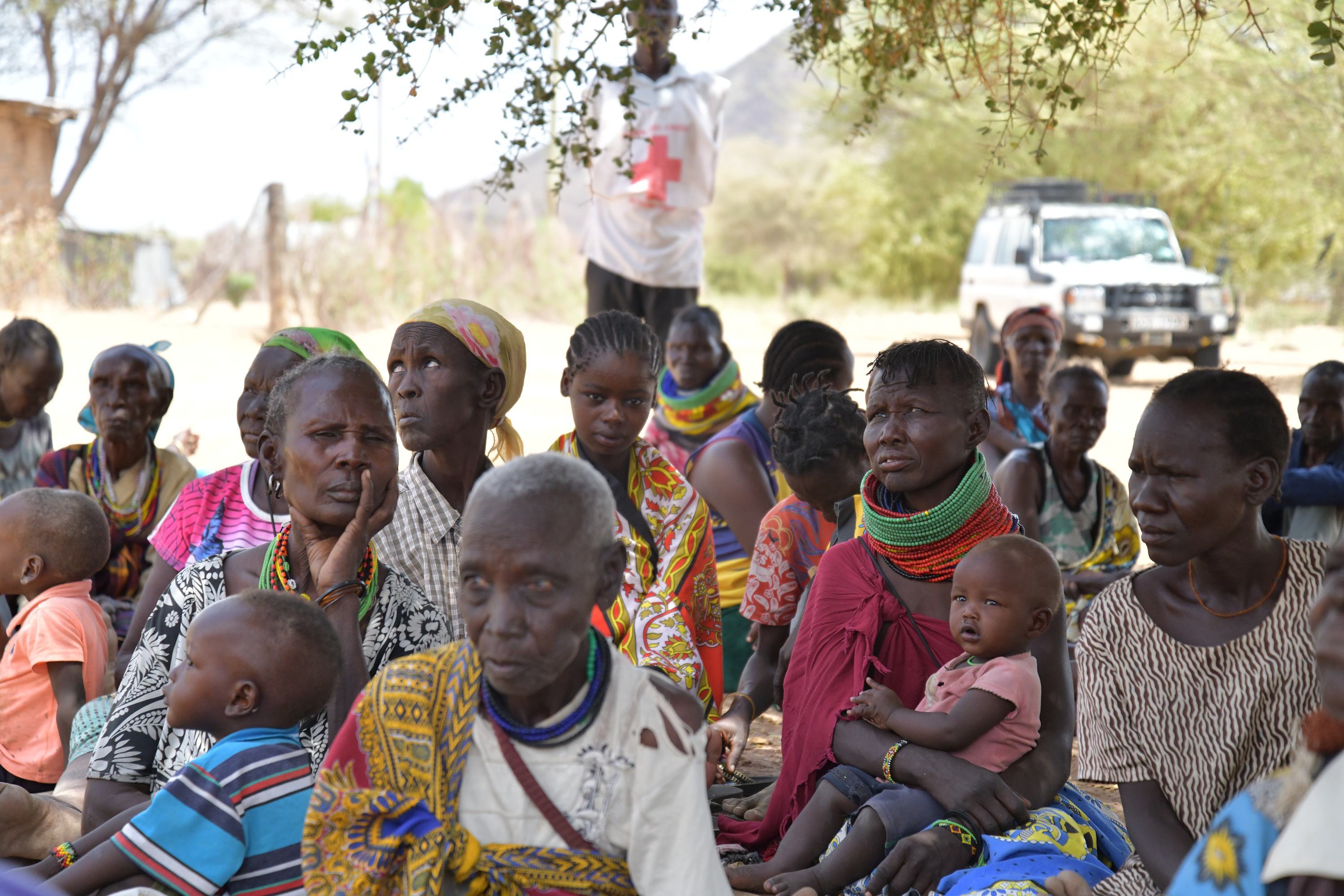 Un groupe de femmes et d'enfants kényans se rassemble à l'extérieur lors d'une opération de secours en cas de sécheresse, avec un employé de la Croix-Rouge et un véhicule d'aide visibles en arrière-plan.