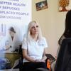 Женщина в белой рубашке-поло МОМ сидит и разговаривает с другим человеком во время консультации, а позади нее висит баннер, посвященный медицинским услугам для украинских беженцев в Молдове.